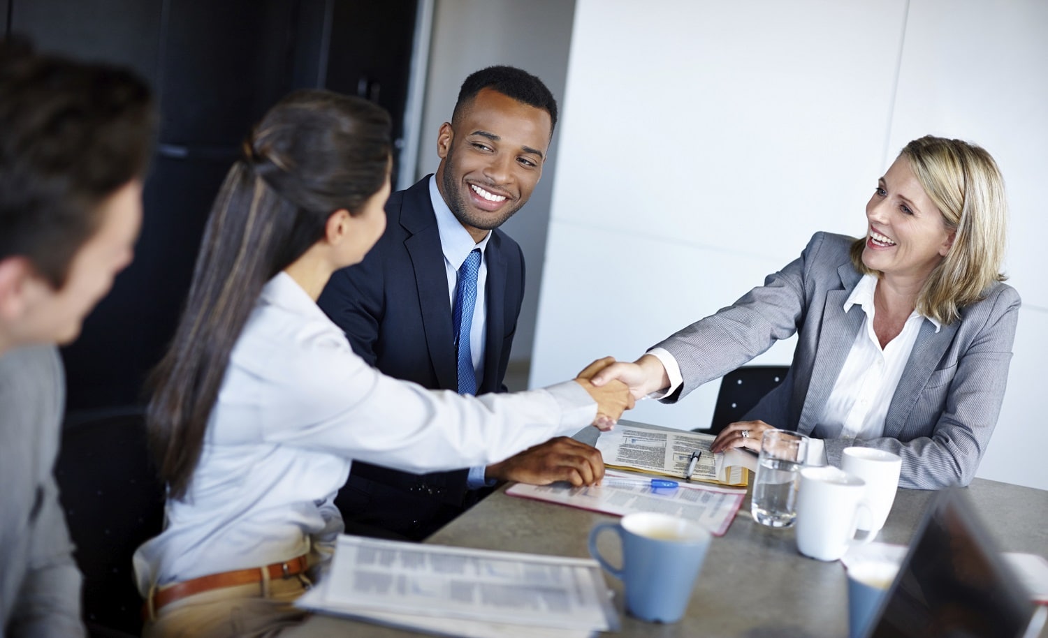 Image of people shaking hands at a desk with four people seated dressed professionally